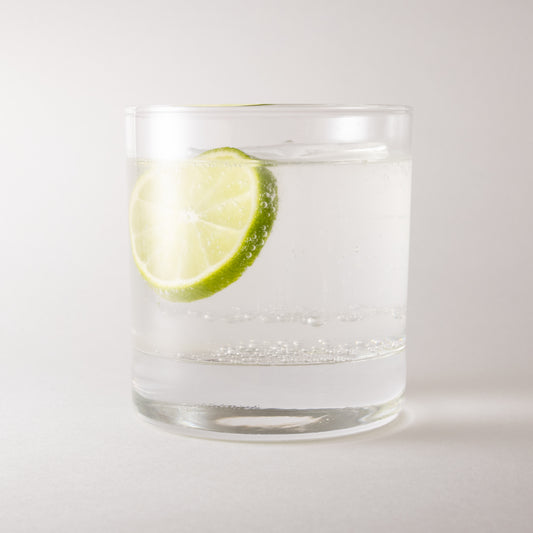 Canoe Candle Co's 12.75oz rocks glass filled with soda and a lime slice on a plain white background.