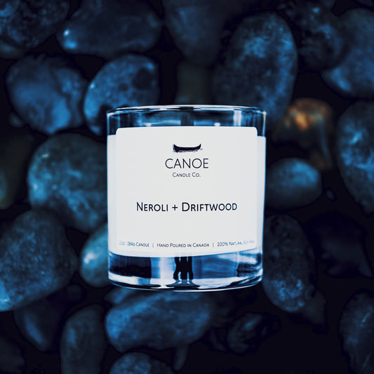 CANOE Candle Co's Neroli + Driftwood 10oz soy wax candle on dark blue river rock